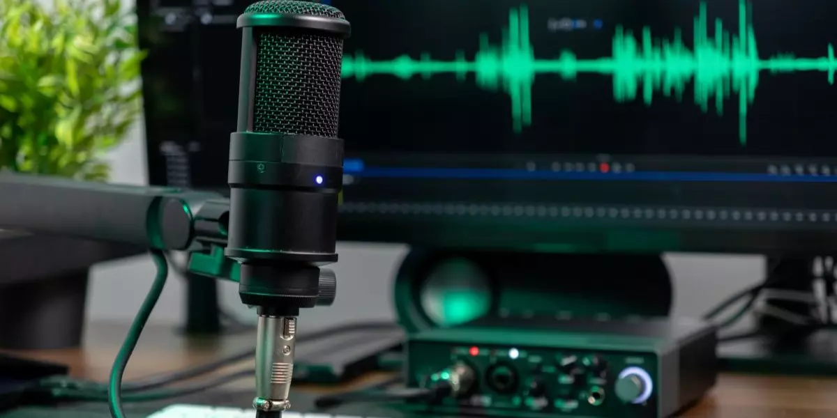 A desk setup with a microphone, audio interface, keyboard and a computer screen
