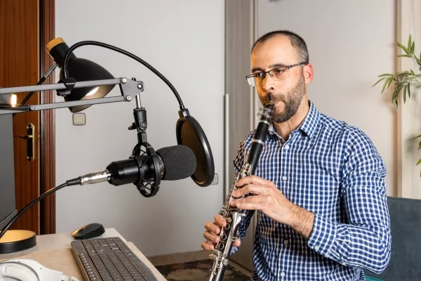 A male adult taking online clarinet lessons from home playing the clarinet into a microphone