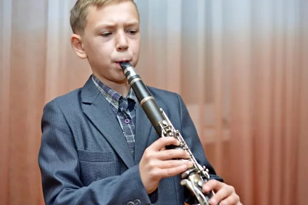 A male child playing the clarinet in a nice suit jacket