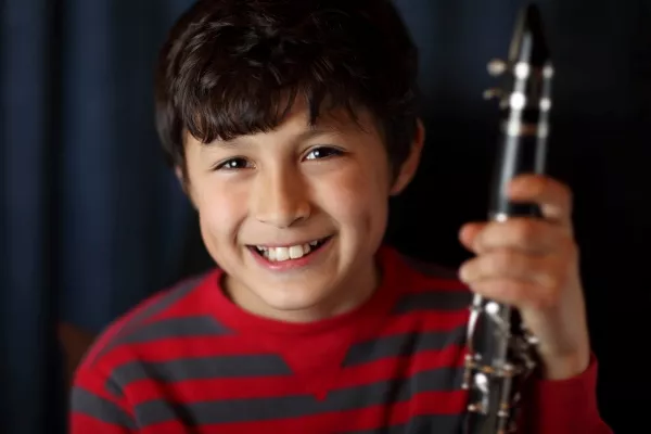A boy smiling at the camera while holding a clarinet