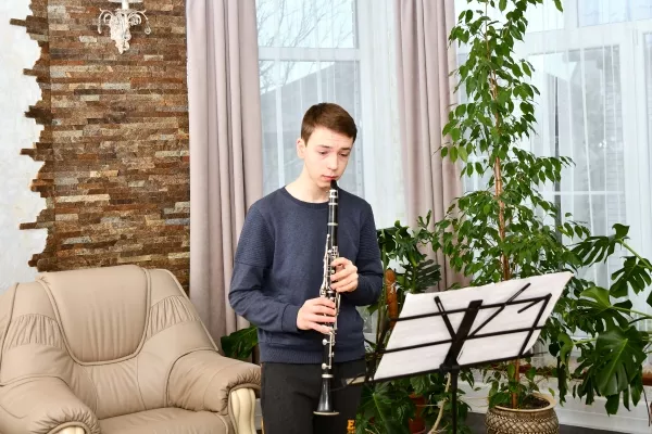 A male teenager playing the clarinet and reading sheet music