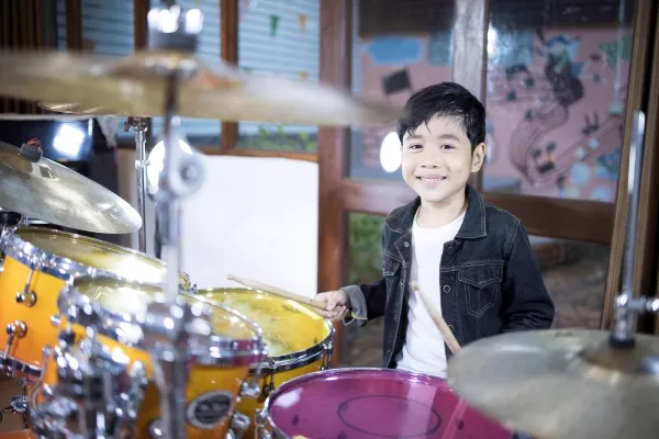 A kid smiling at the camera playing drums