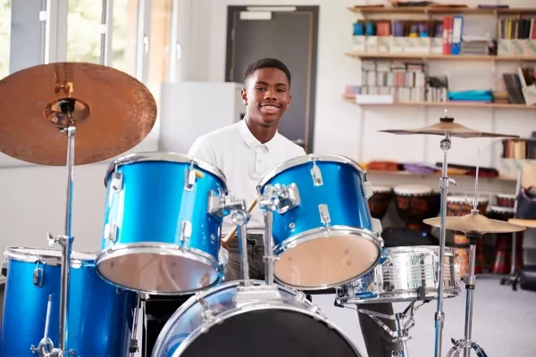 Teenager smiling at the camera behind a drum kit