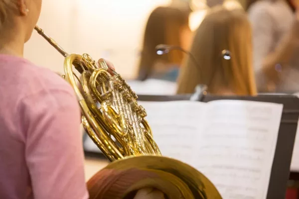 A shoulder view of an adult woman playing the french horn reading from sheet music