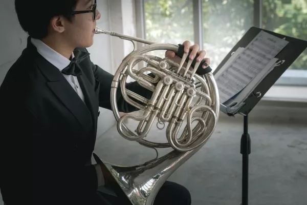 Teenager playing the French Horn in a suit and reading sheet music