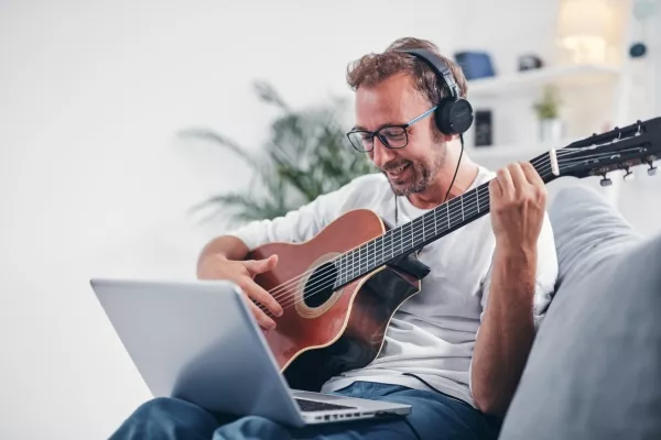 An adult male taking online Guitar Lessons on his laptop