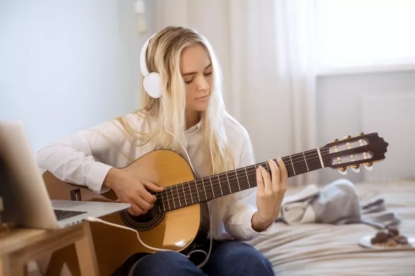 A female teen playing Guitar with headphones plugged into her laptop