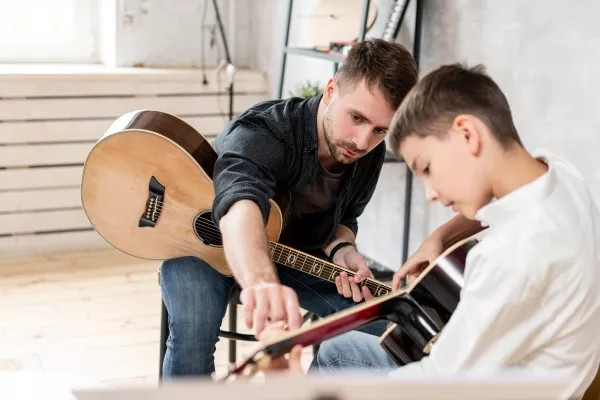 A male child taking guitar lessons with a teacher