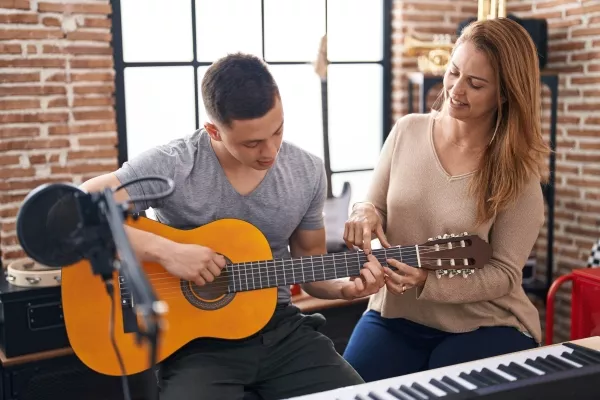 A male teen taking private guitar lessons with a female instructor