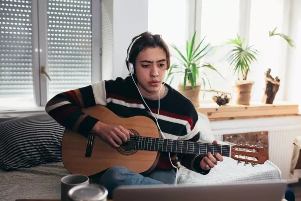 A female with a laptop & headphones taking online guitar lessons