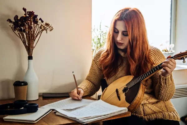 A female writing notes while holding the mandolin at home