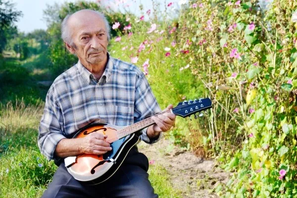 A senior man playing the mandolin outside in his garden