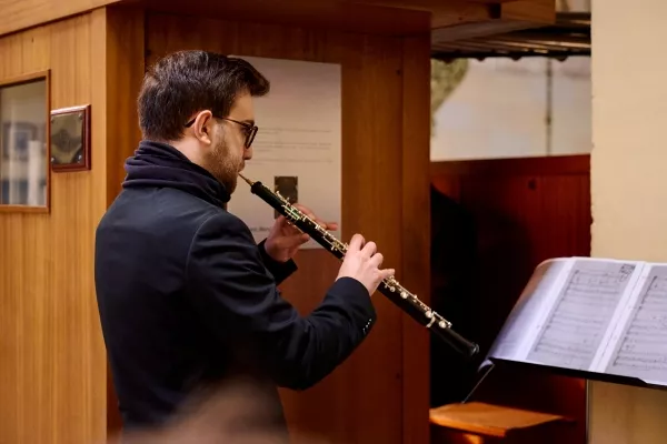 An adult male playing the oboe while reading sheet music