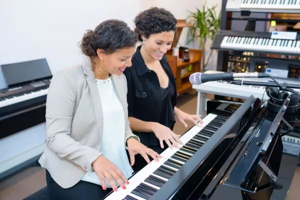two adult women smiling while playing piano together
