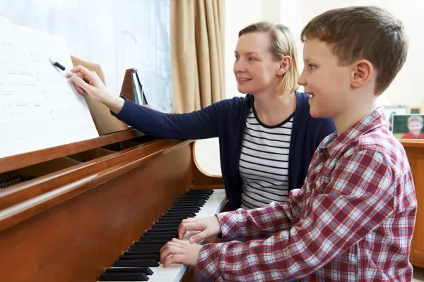 A child playing the piano while his teacher points at the next note to play on the music sheet