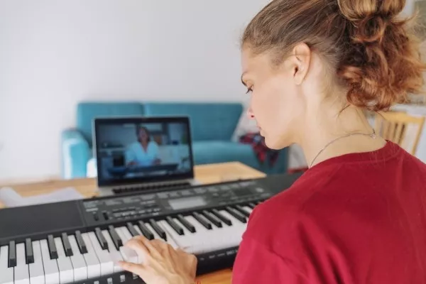 A woman with an laptop in front of her during a zoom call taking an online piano lesson