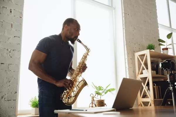 An adult man playing the saxophone in front of his laptop during an online saxophone lesson