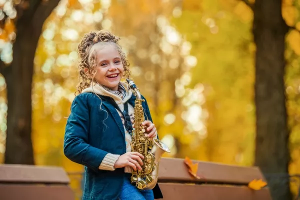 female child smiling at the camera while holding a saxophone outside
