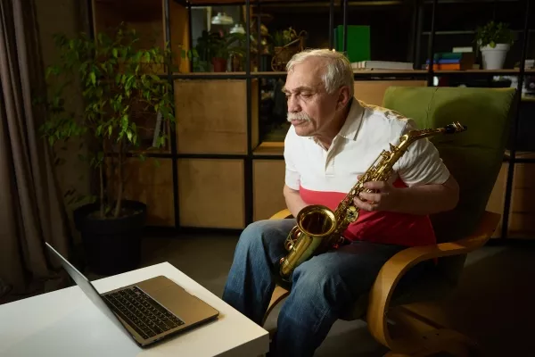 A senior man sitting on his couch in front of his laptop taking online Saxophone Lessons at home