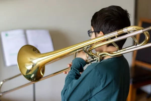 A child reading sheet music while playing the trombone at home