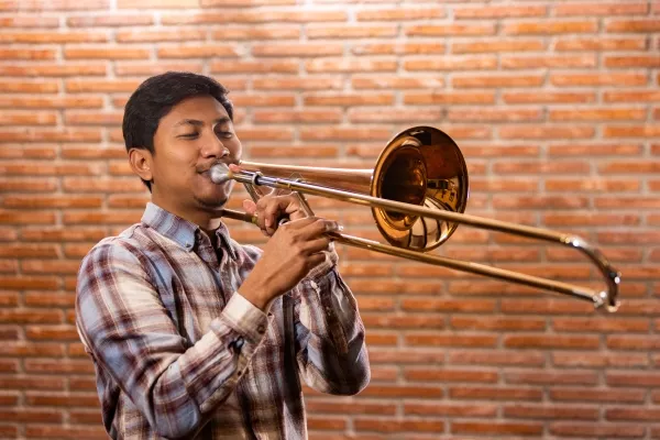 Teenager playing the trombone with a brick wall in the background
