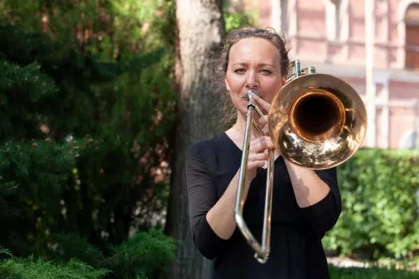 female adult playing the trombone outdoors looking at the camera