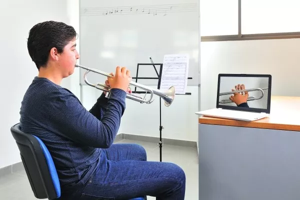 A teen with his laptop during a zoom call taking an online trumpet lesson