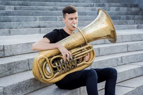 A male playing the Tuba outside sitting on some stairs