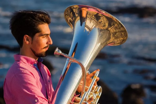A man playing the tuba outside with an ocean in the background