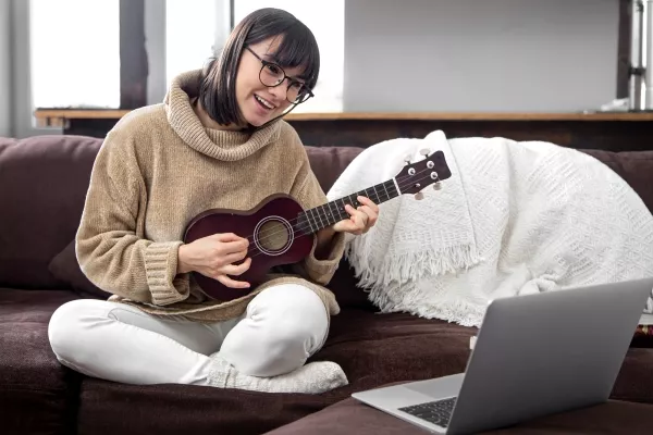 A female on the couch with her laptop taking online Ukulele lessons on video