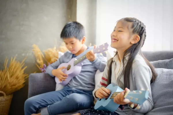 Two sibling children on the couch playing ukulele together