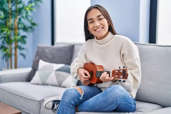 A female teen playing the Ukulele at home on the couch