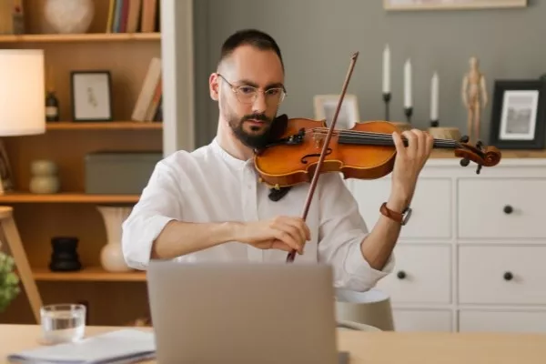 Adult male taking online violin lessons playing on his laptop