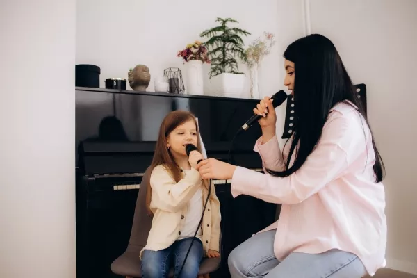 A childing learning to hold a microphone with a teacher